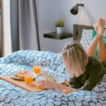 Жена закусва в леглото, легнала по корем